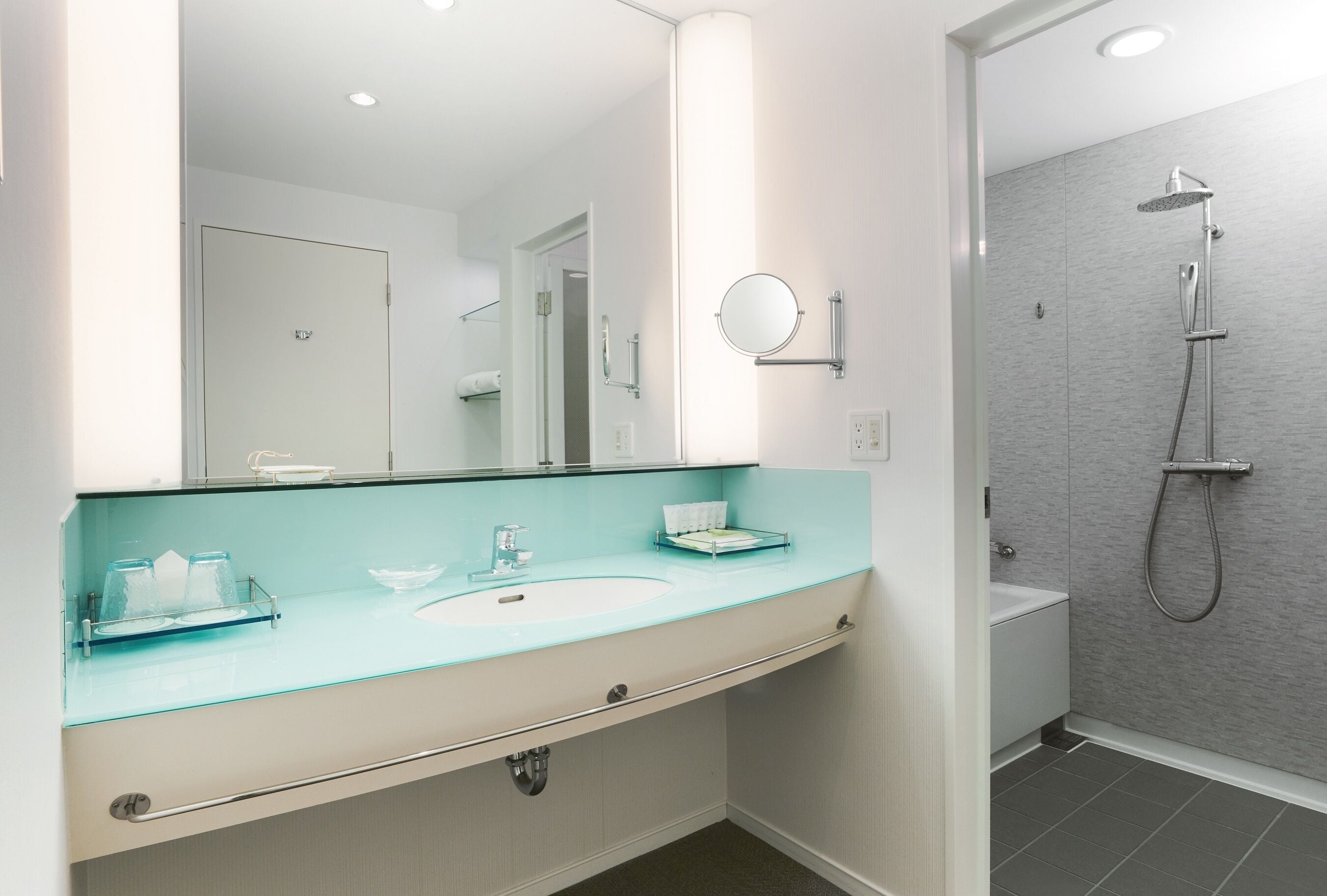 A modern bathroom with a glass sink, a round mirror, and a shower area.
