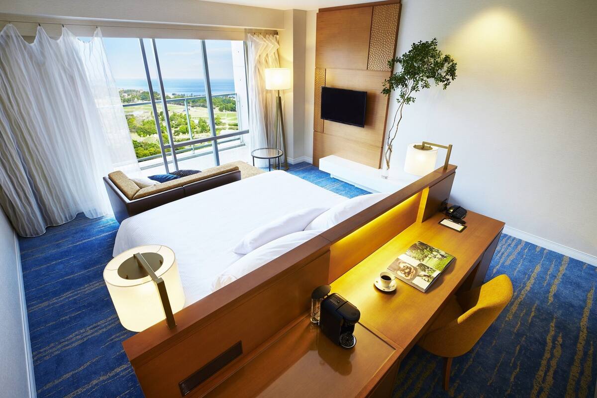 Habitación de hotel con una cama grande, un escritorio con silla, televisor montado en la pared y vista al exterior.
