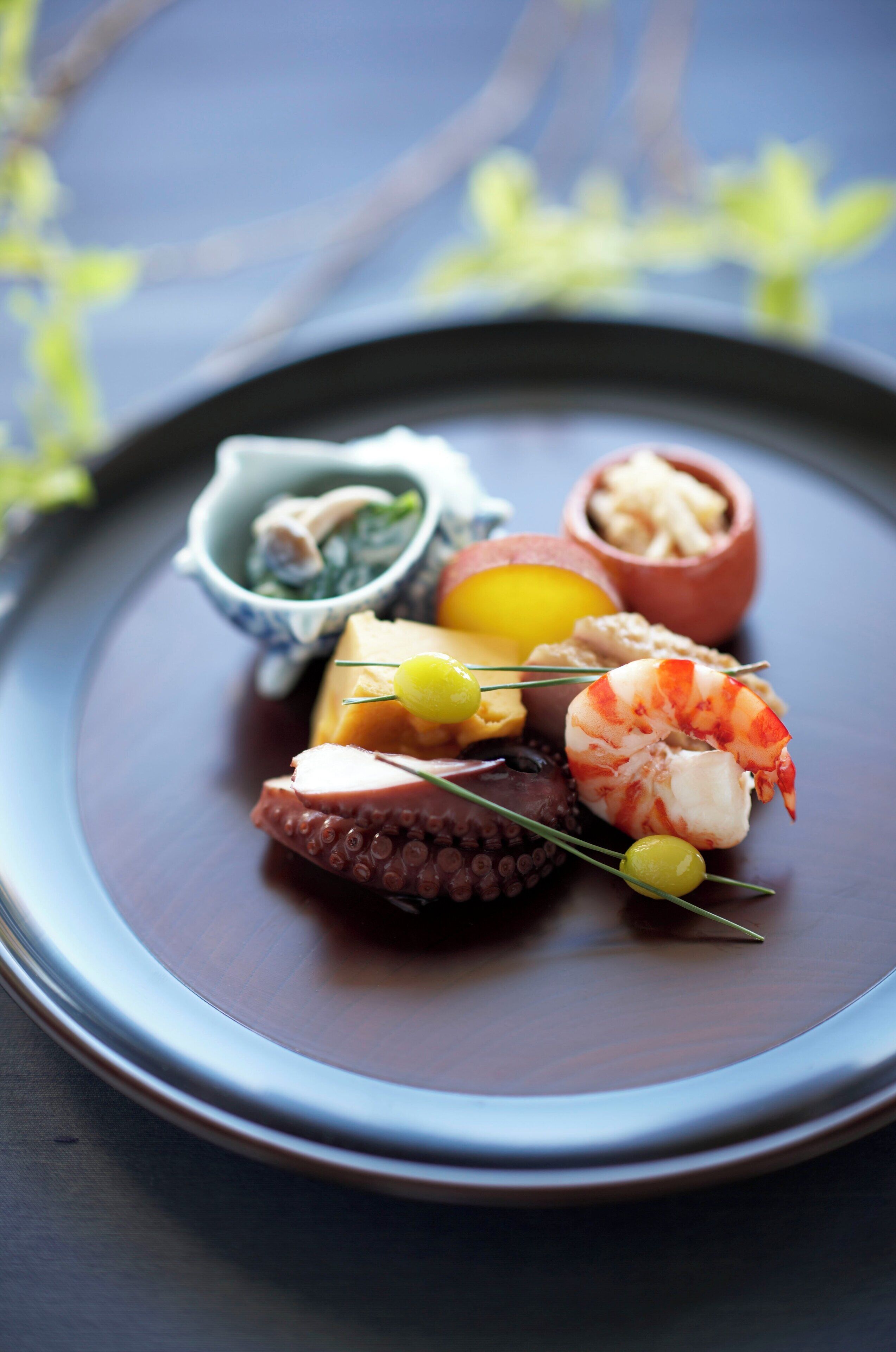 A plate with various seafood items including shrimp, octopus, and a small bowl of greens.