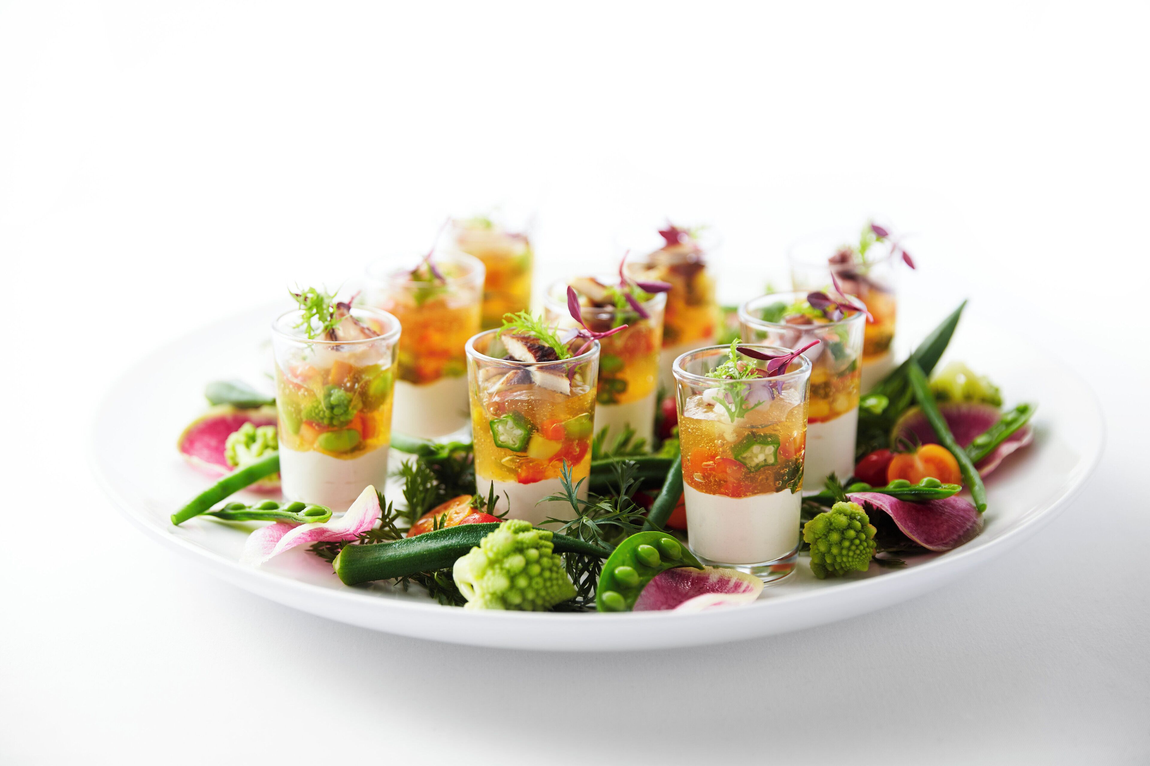 A white plate with several clear glasses containing layered food and garnishes.