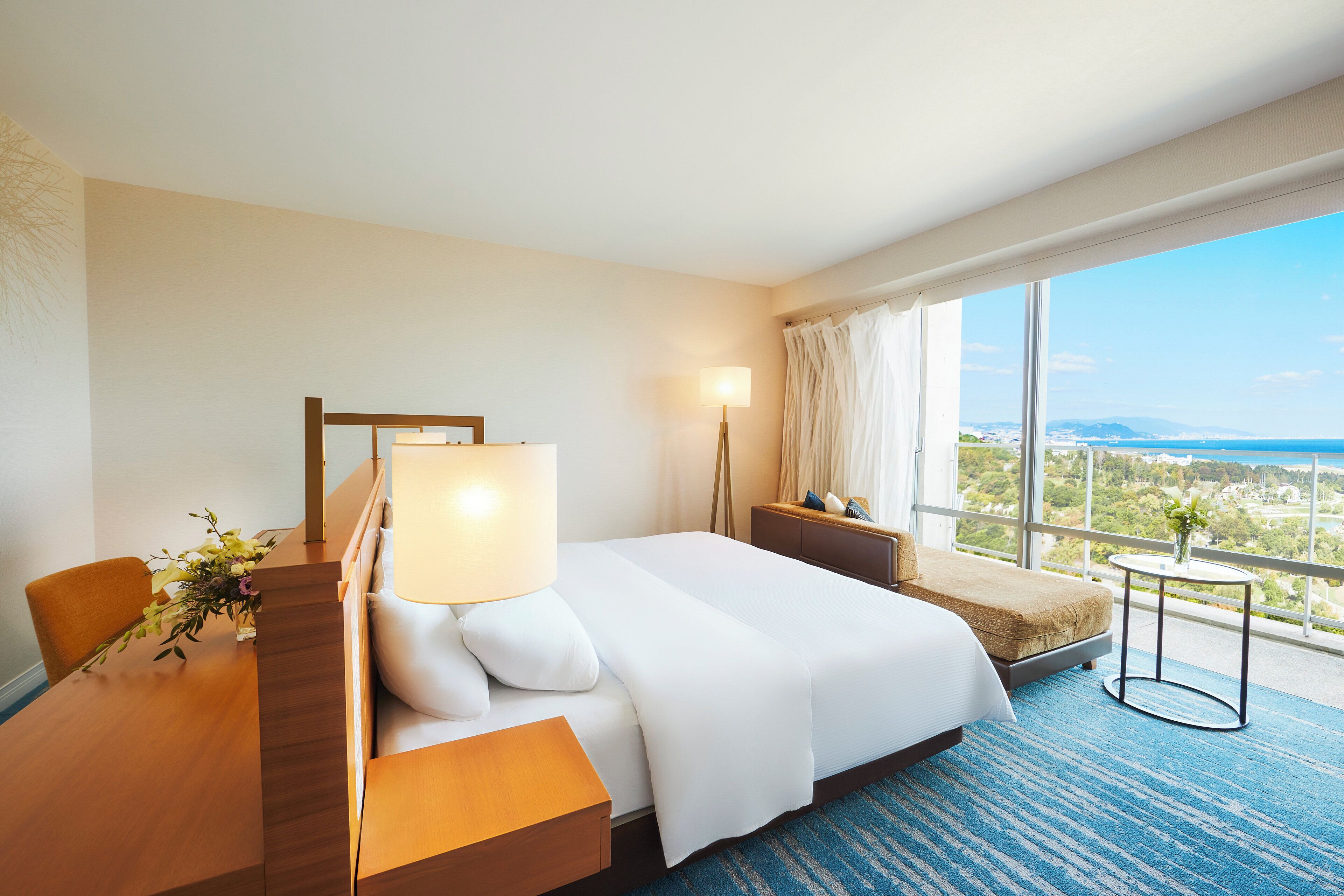 Hotelkamer met een groot bed, een bureau met lamp, een stoel en uitzicht op de oceaan.