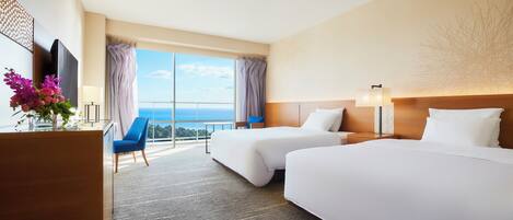 A hotel room with two beds, a desk, a chair, and a large window offering a view.