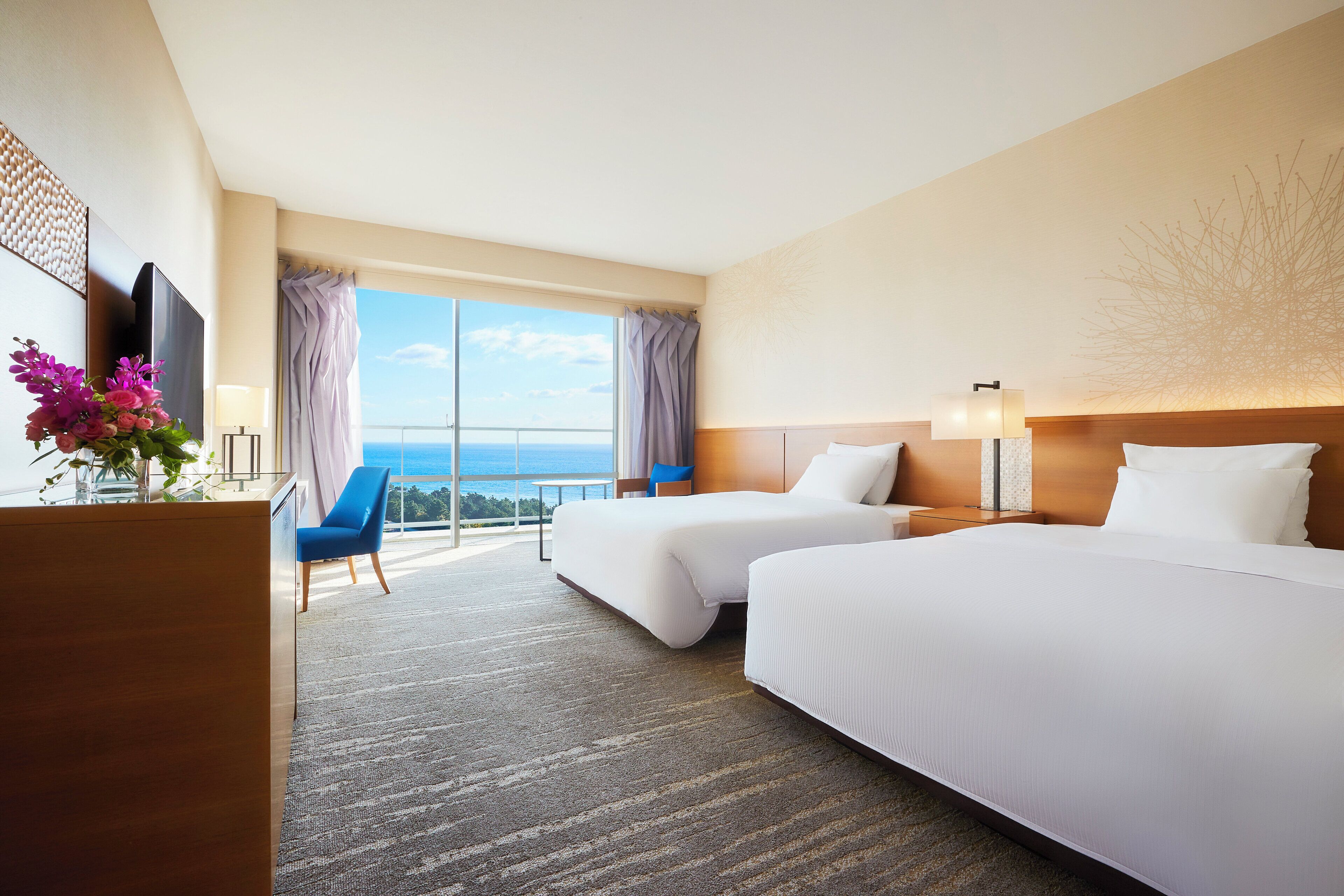 Habitación de hotel con dos camas, un escritorio, una silla, un televisor y un ventanal con vistas.