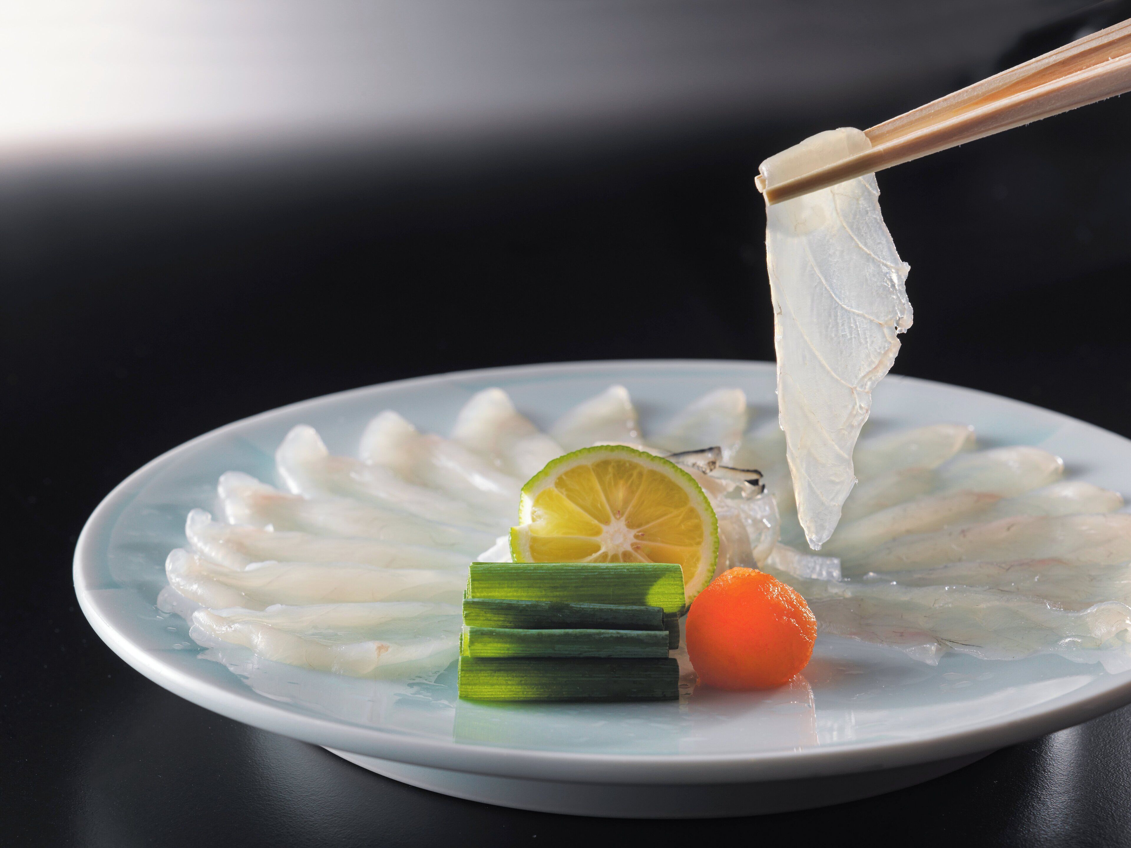 A plate of sashimi with a lime wedge and a small orange slice.
