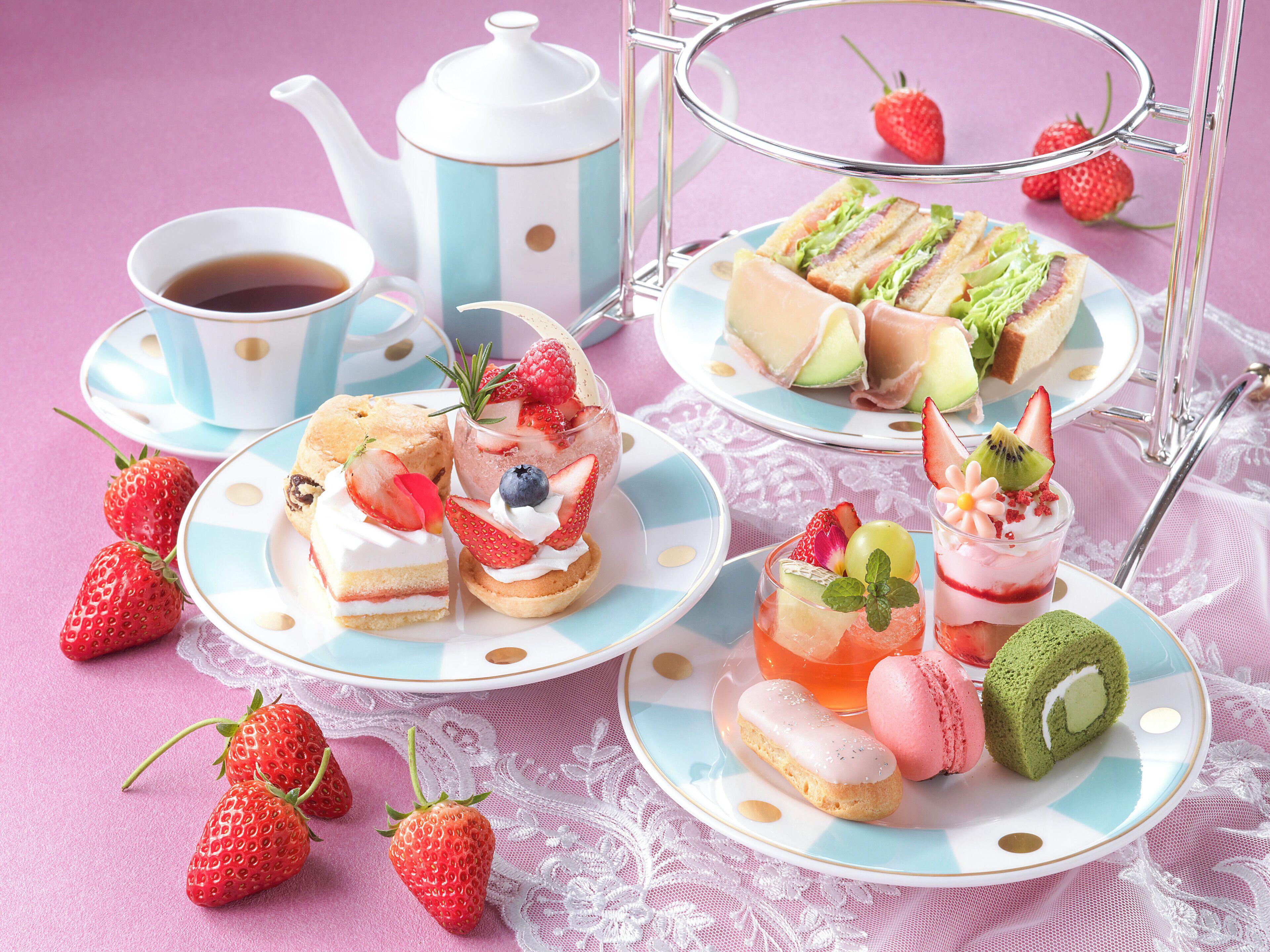A variety of desserts and a teapot on a table with a lace tablecloth.
