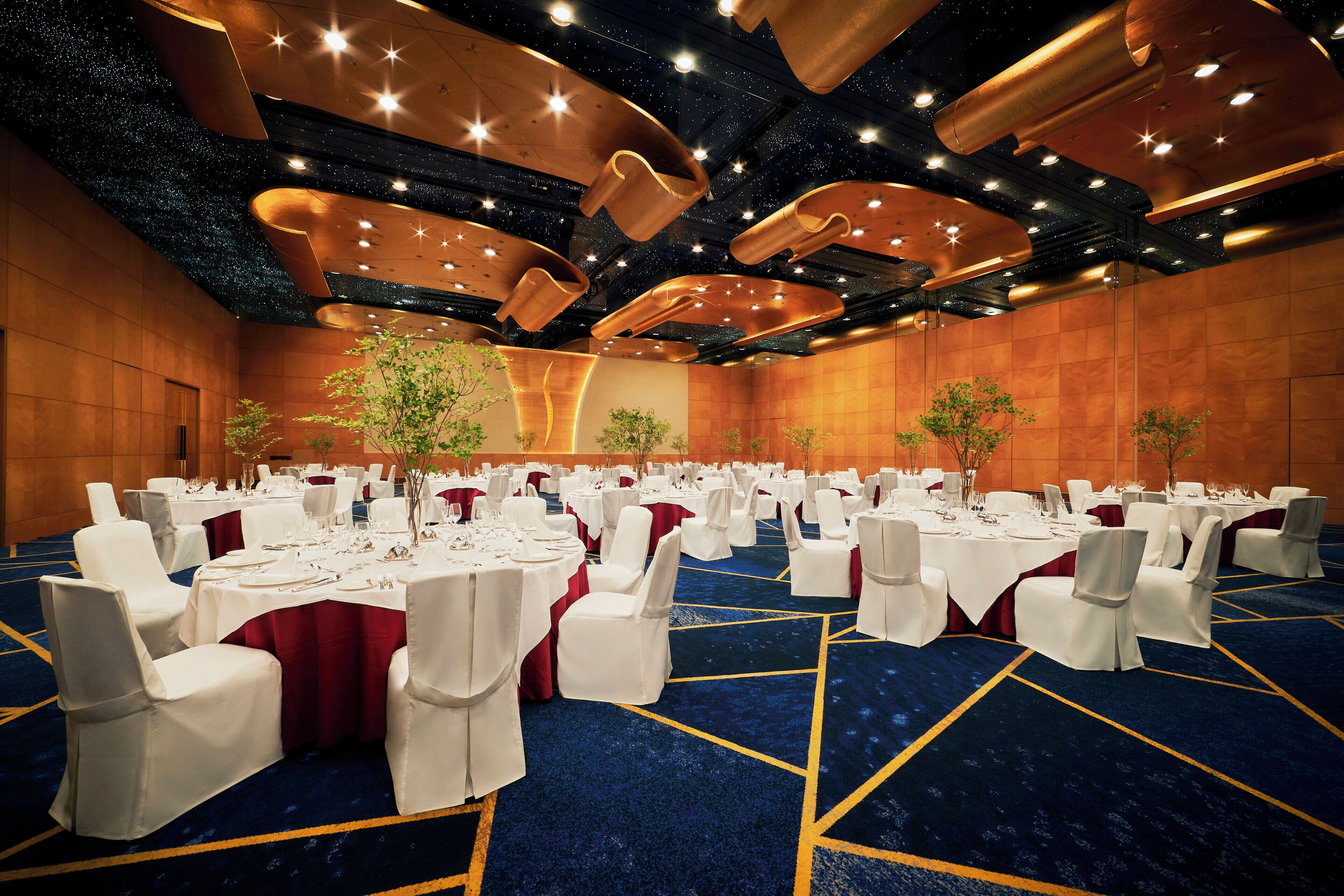 A large conference room with round tables, white chairs, and red tablecloths.