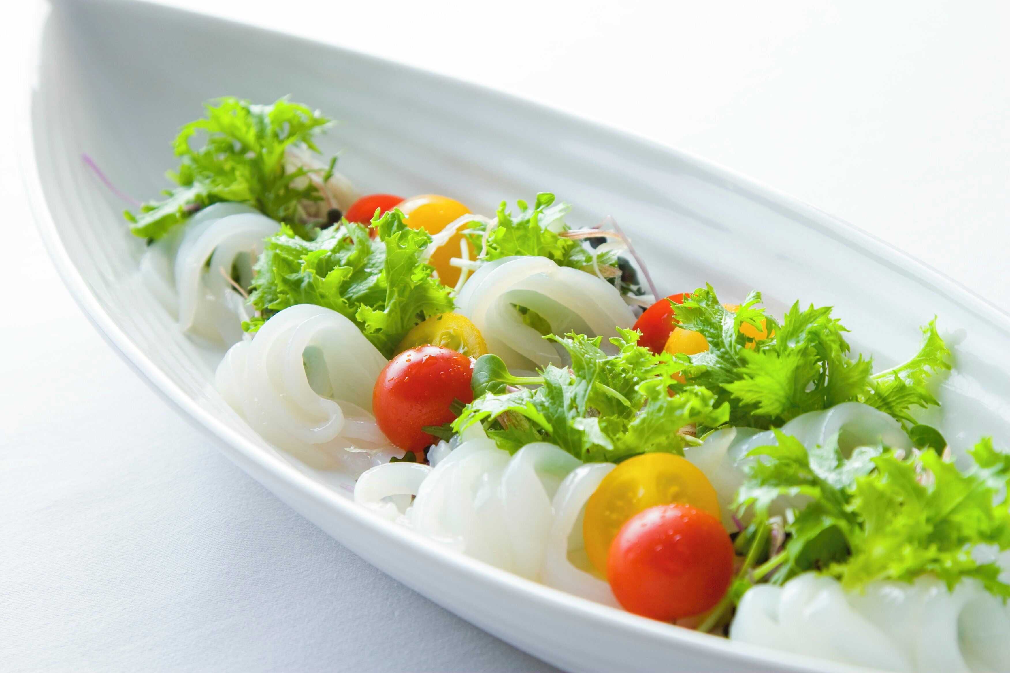 A white oval plate with a salad consisting of lettuce, cherry tomatoes, and possibly onions.