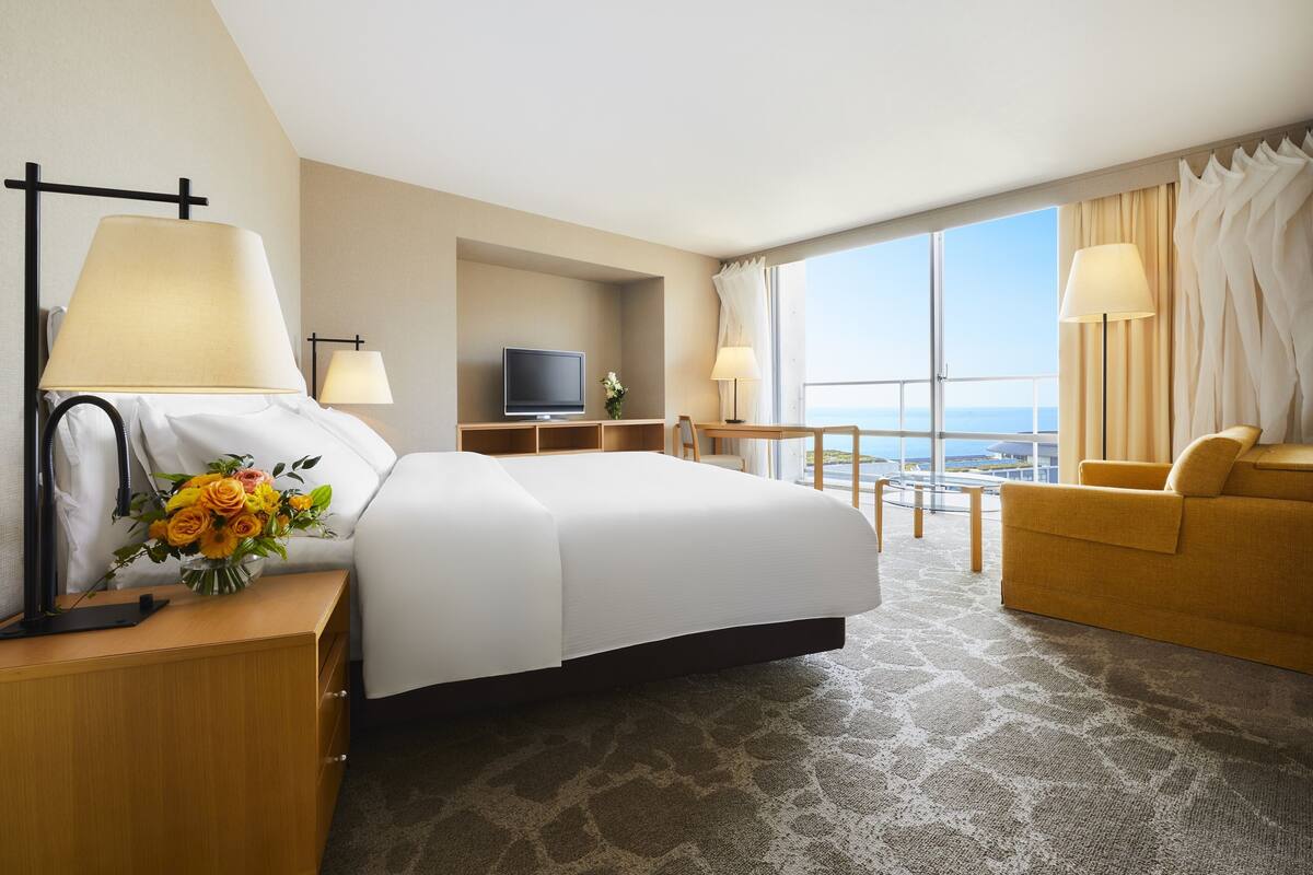 Habitación de hotel con una cama grande, un escritorio, televisión, sofá y vista al océano.