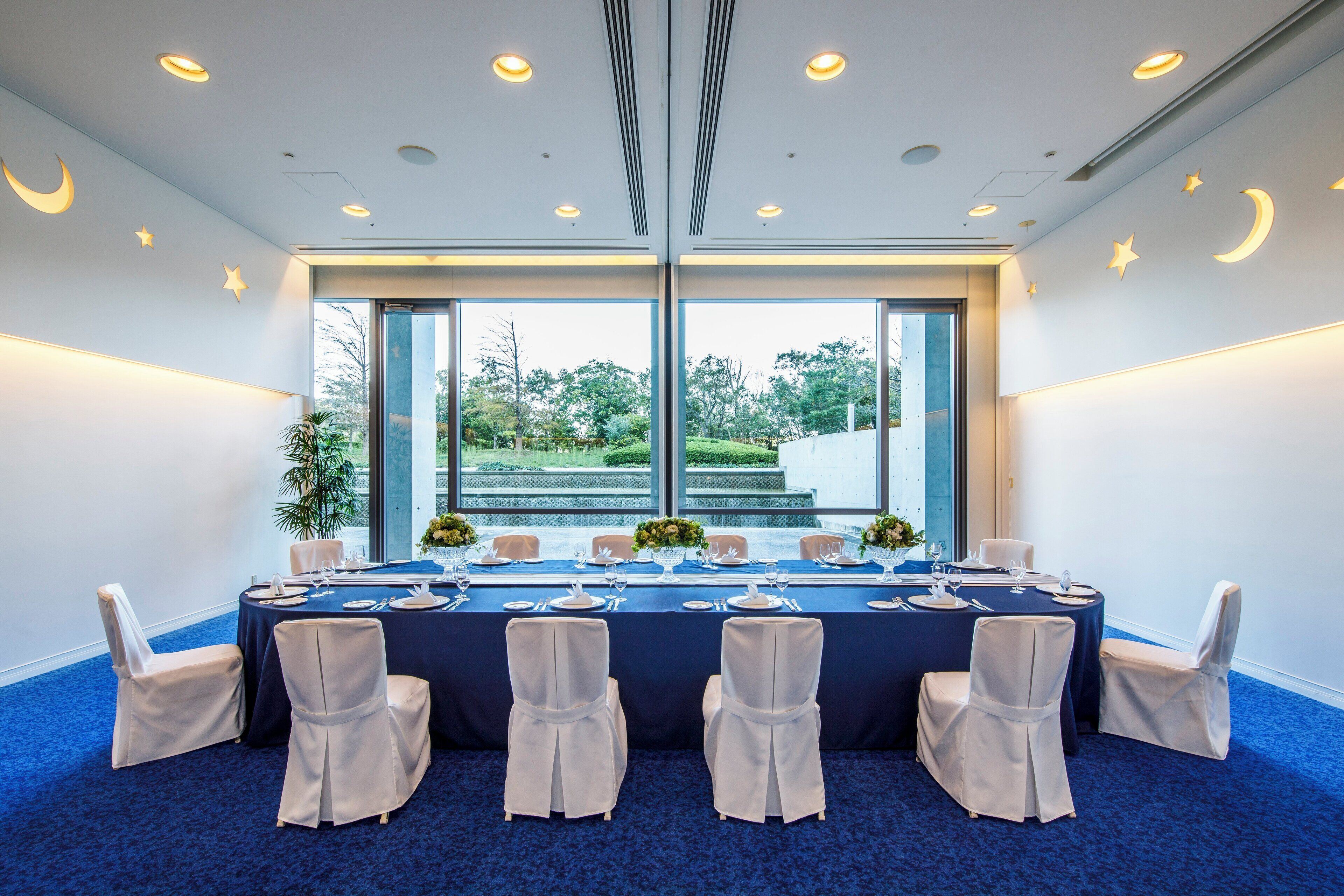 A conference room with a long table set for a meeting, large windows, and a view of the outdoors.