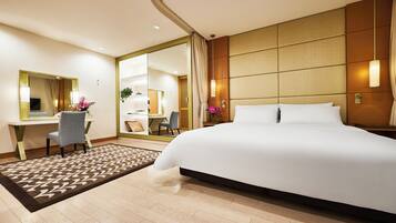A hotel room with a large bed, a desk with a chair, a mirror, and a view of the bathroom.