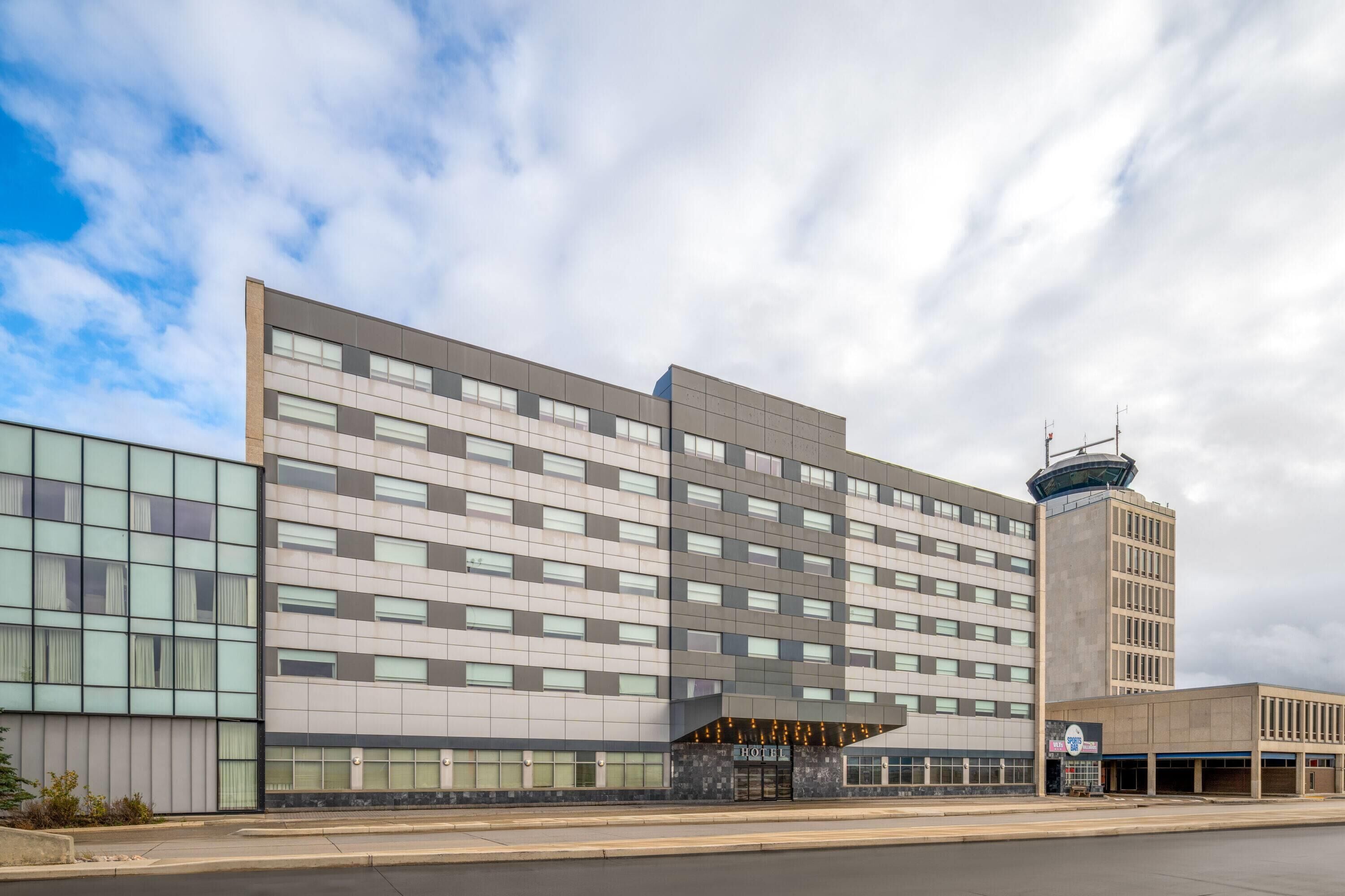 A modern hotel with a large, multi-story structure, featuring a prominent entrance with a glass facade and a control tower on the right.