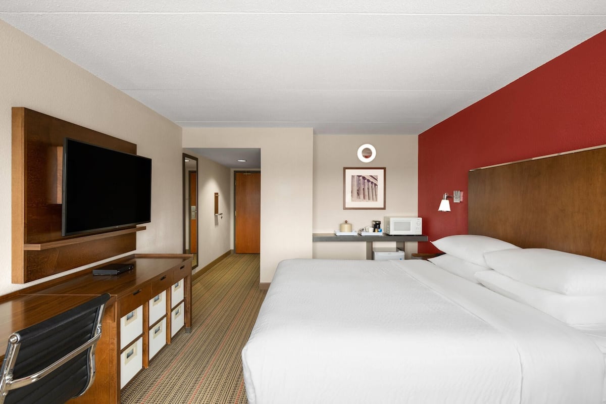 Habitación de hotel con una cama grande, un escritorio con televisor de pantalla plana, un microondas y una pequeña mesa con lámpara.