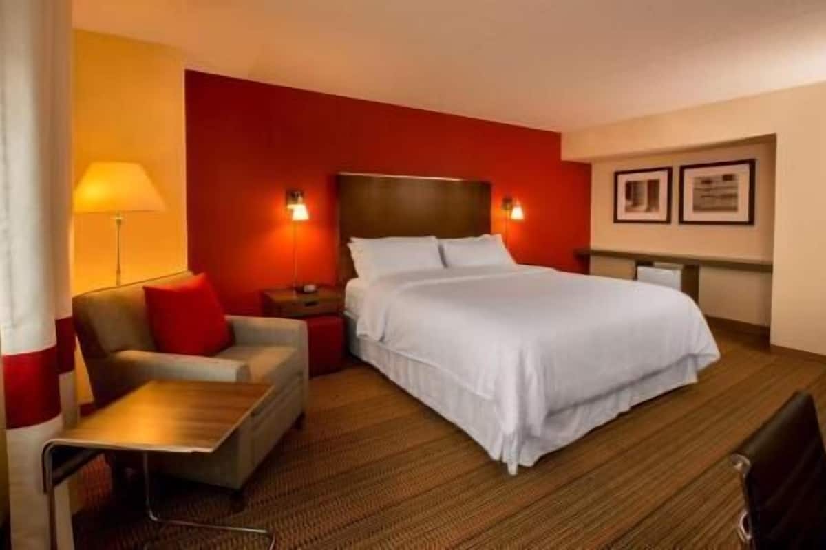 A hotel room with a bed, a desk, a chair, a lamp, and two wall-mounted lights.