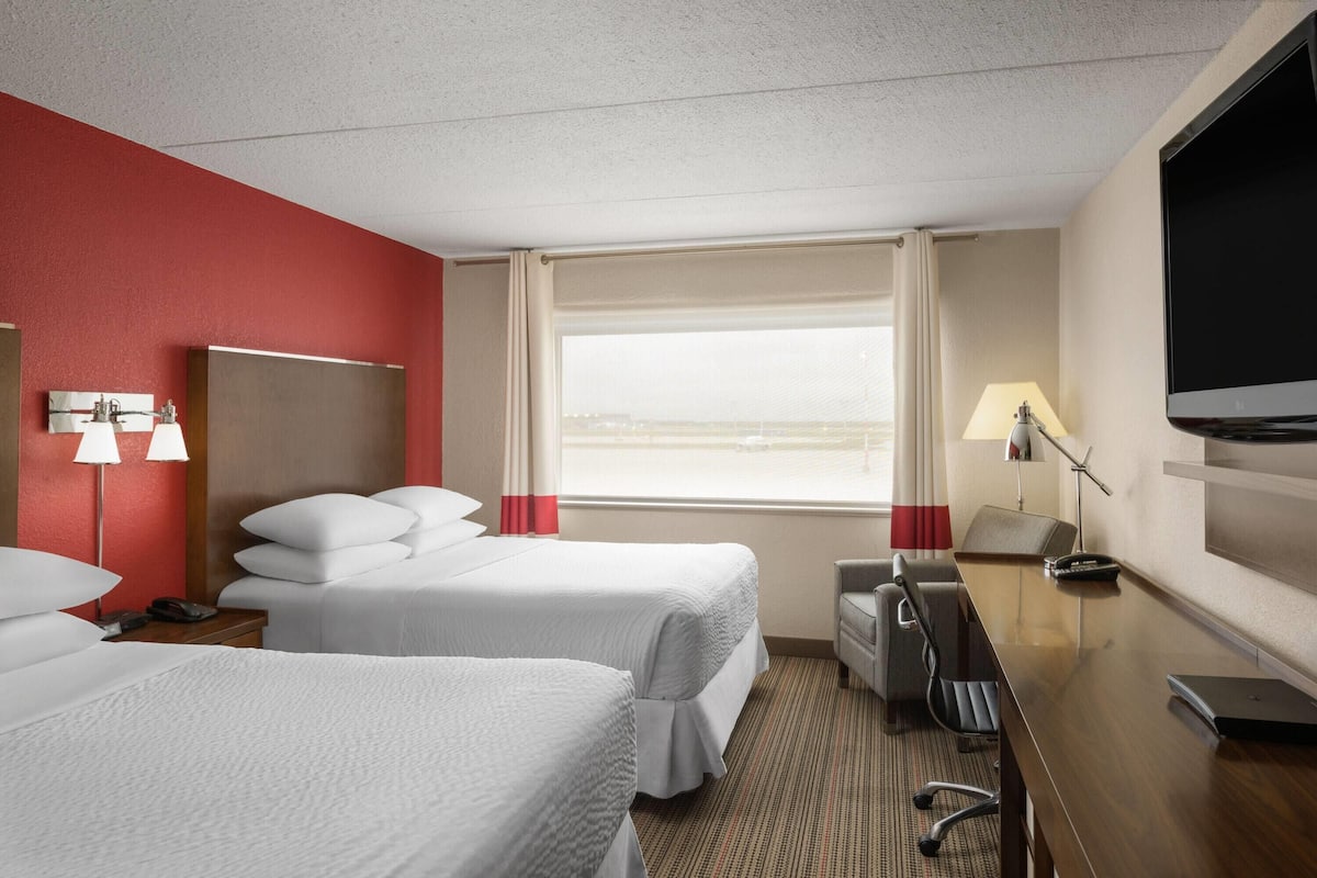 Habitación de hotel con dos camas, un escritorio, un televisor y una ventana con vistas.