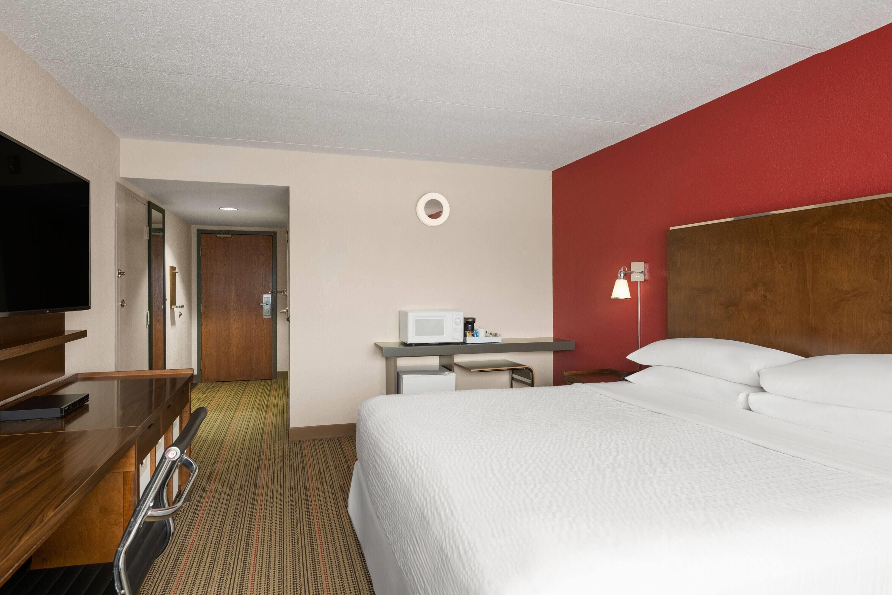 A hotel room with a bed, a desk with a computer, a TV, and a microwave.