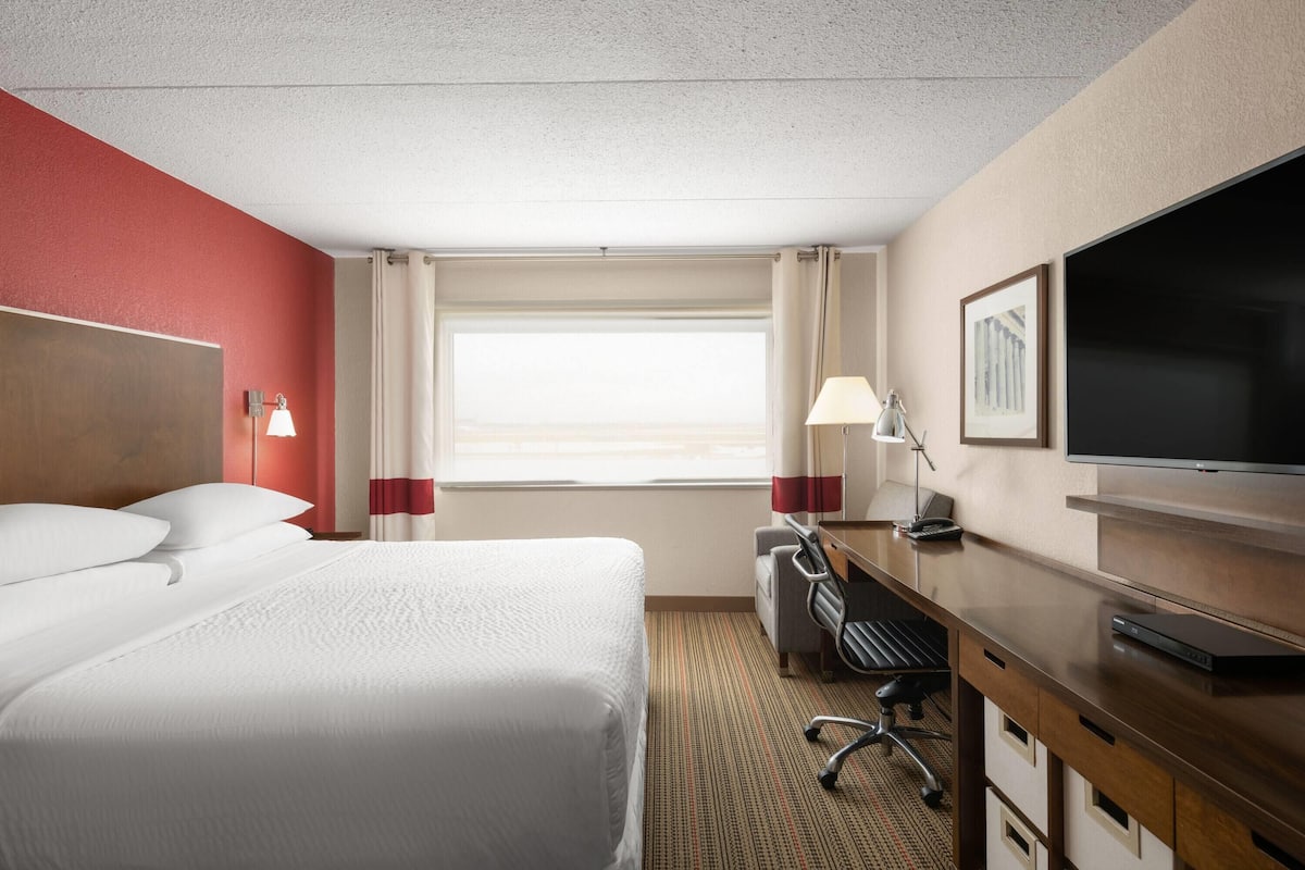 Una habitación de hotel con una cama grande, un escritorio con computadora, un televisor y una ventana con cortinas.