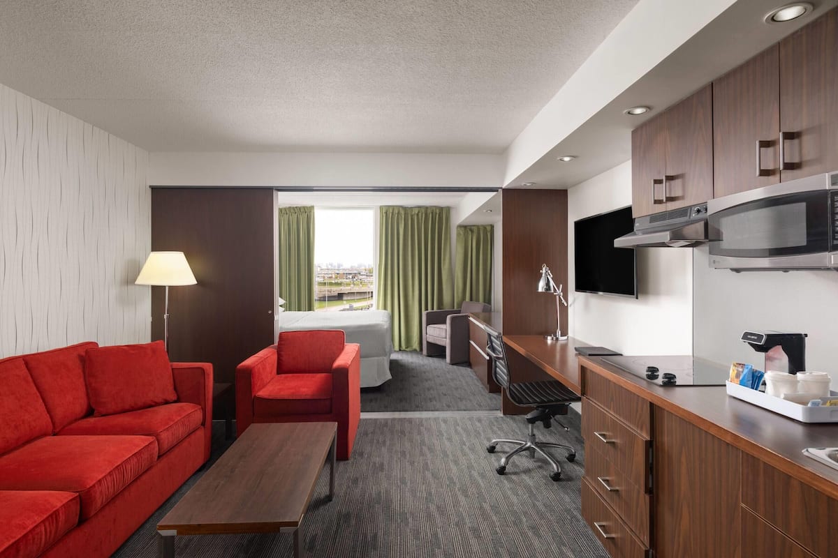 Habitación de hotel con un sofá rojo, un escritorio con computadora, un microondas y un televisor.