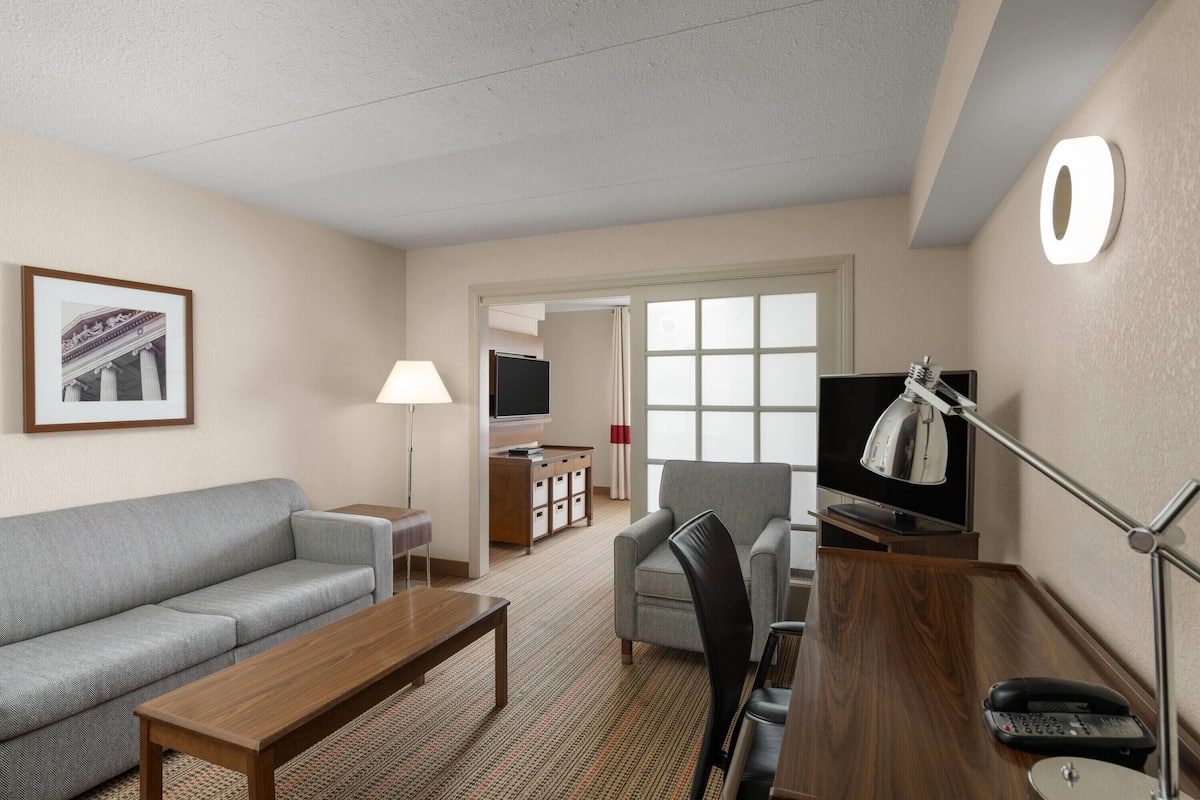 Habitación de hotel con sofá, una mesa de madera, escritorio con teléfono, lámpara y televisión.