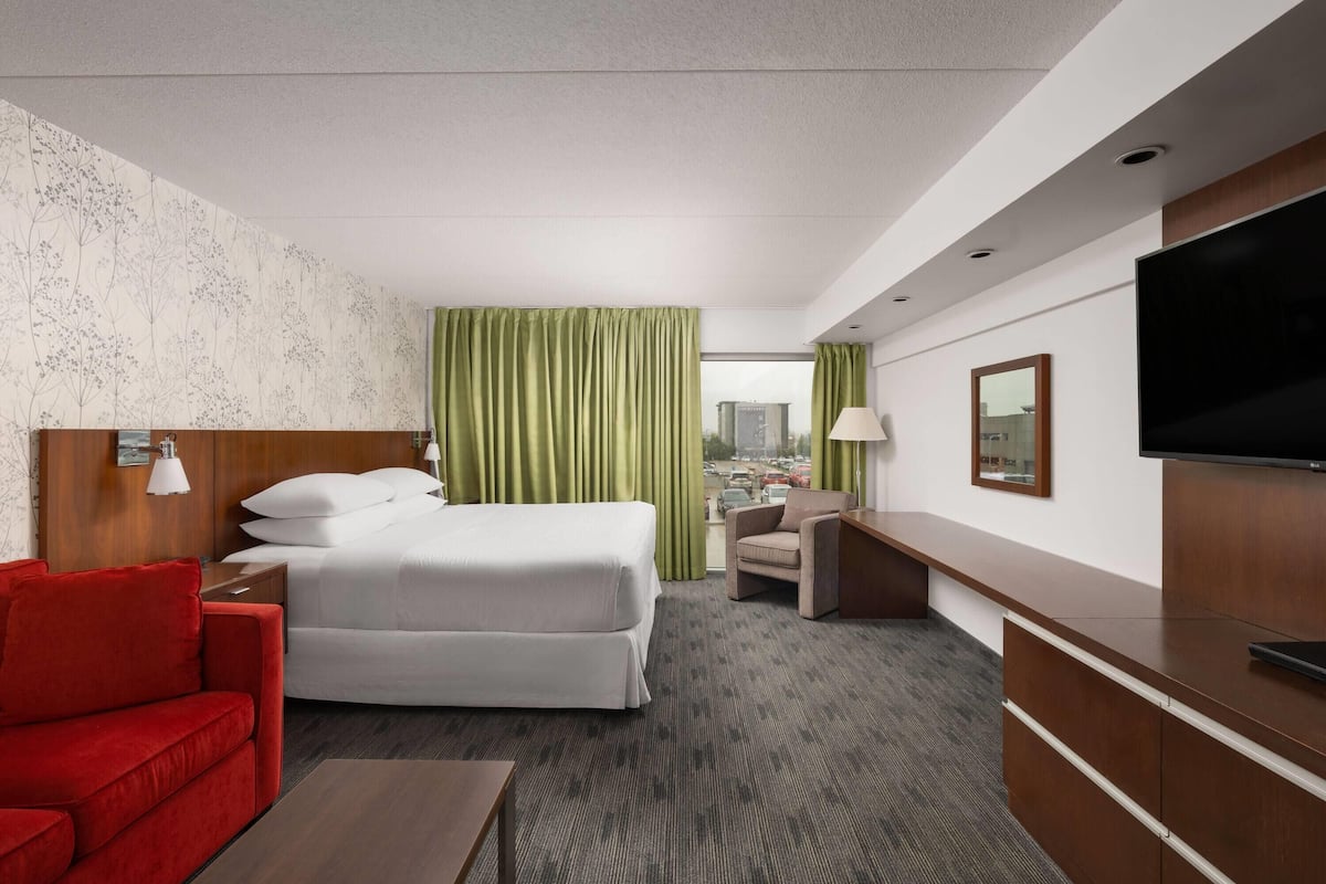 Una habitación de hotel con una cama, un sofá rojo, un escritorio, un televisor y vistas a la ciudad.