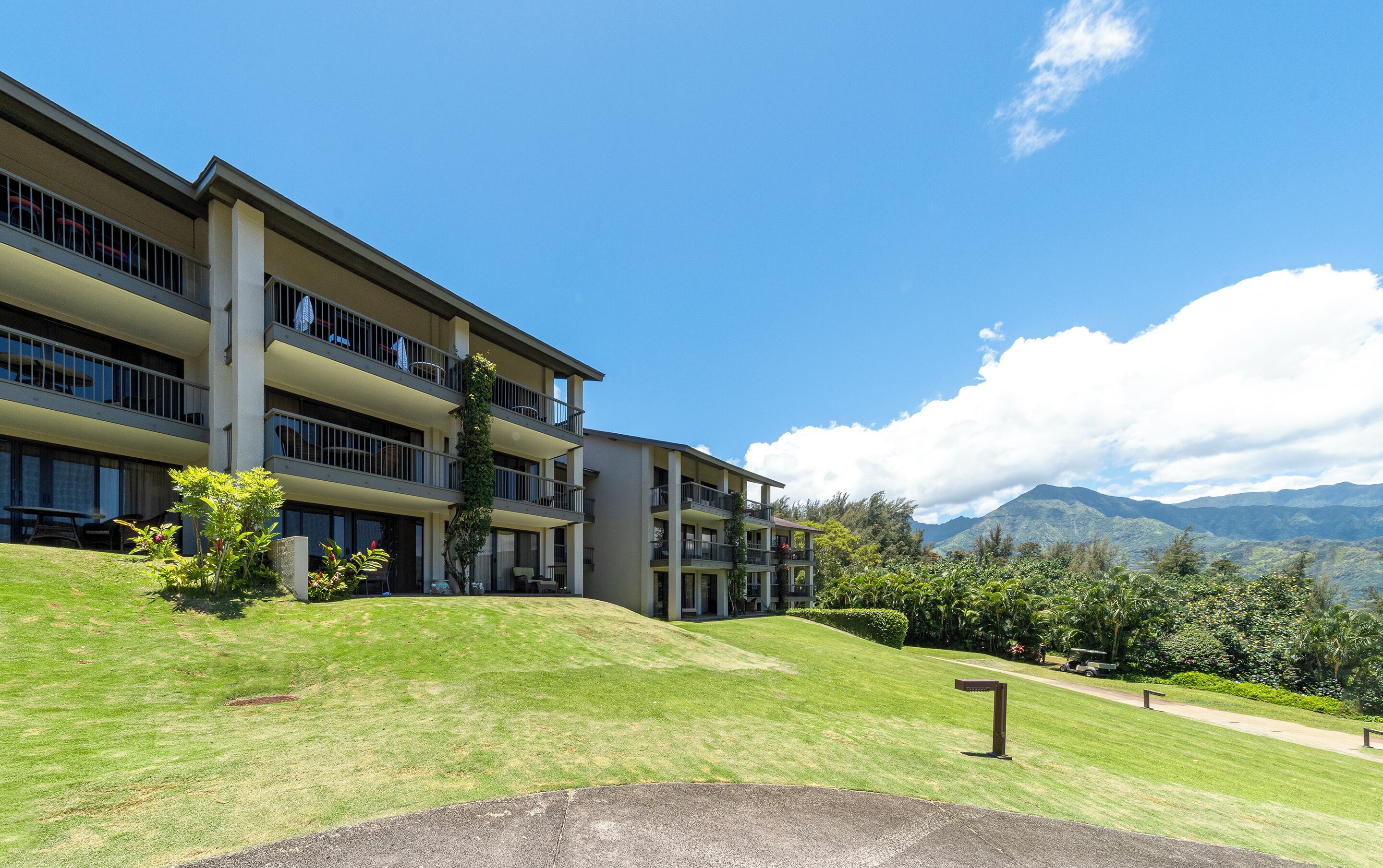 A multi-story hotel with balconies, a well-maintained lawn, and a mountain view.