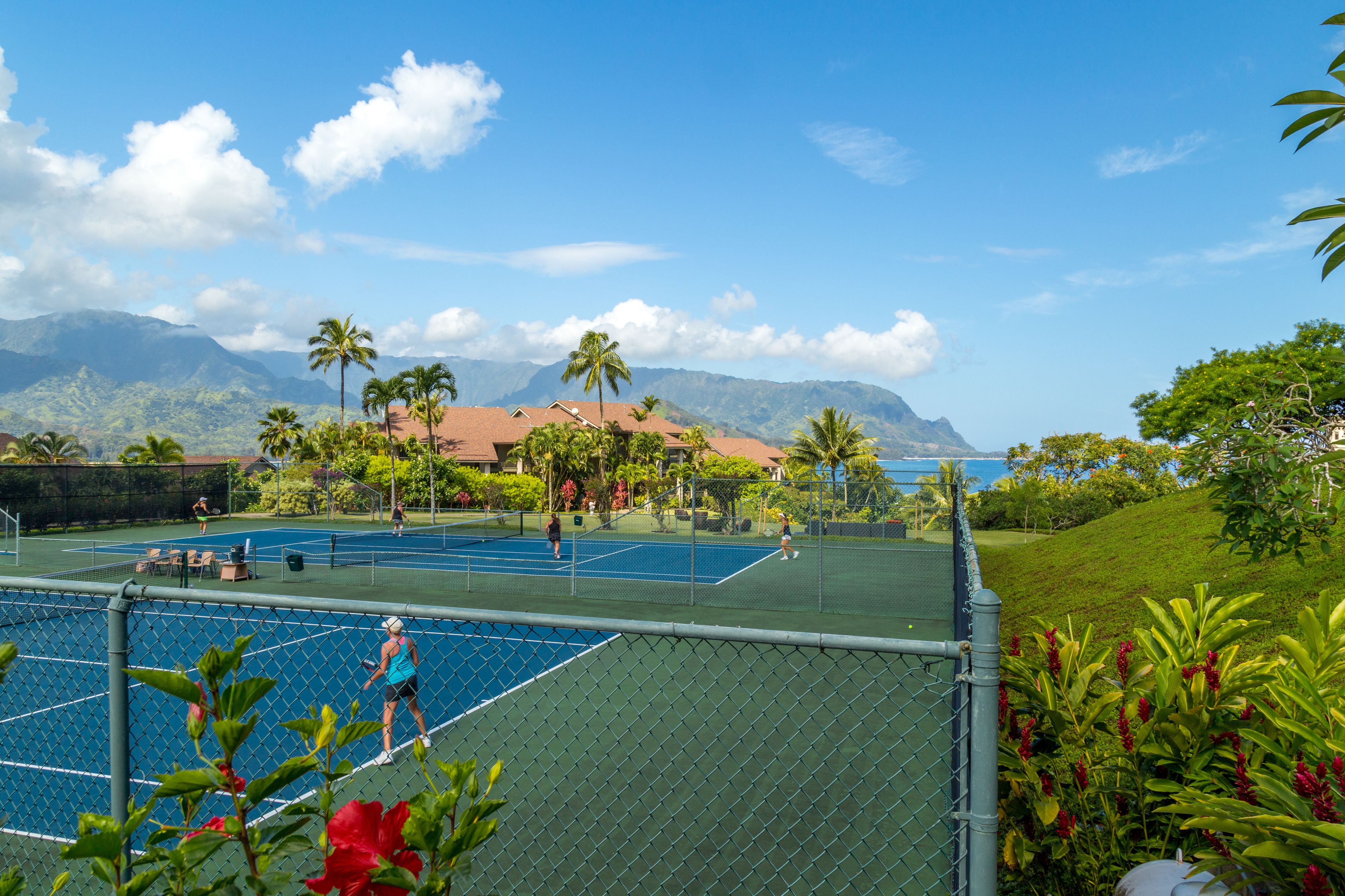 Un court de tennis offrant une vue sur les montagnes et l’océan.
