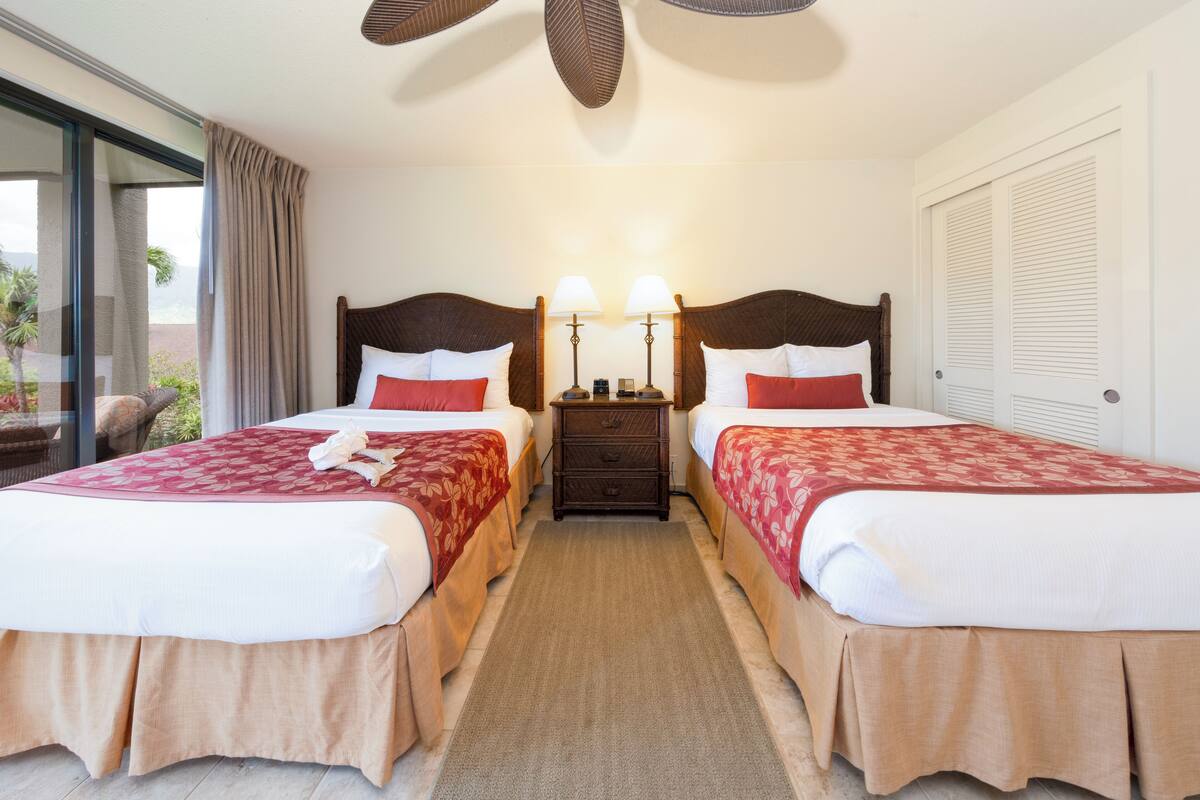 A hotel room with two beds, a nightstand with lamps, and a view of the outdoors.