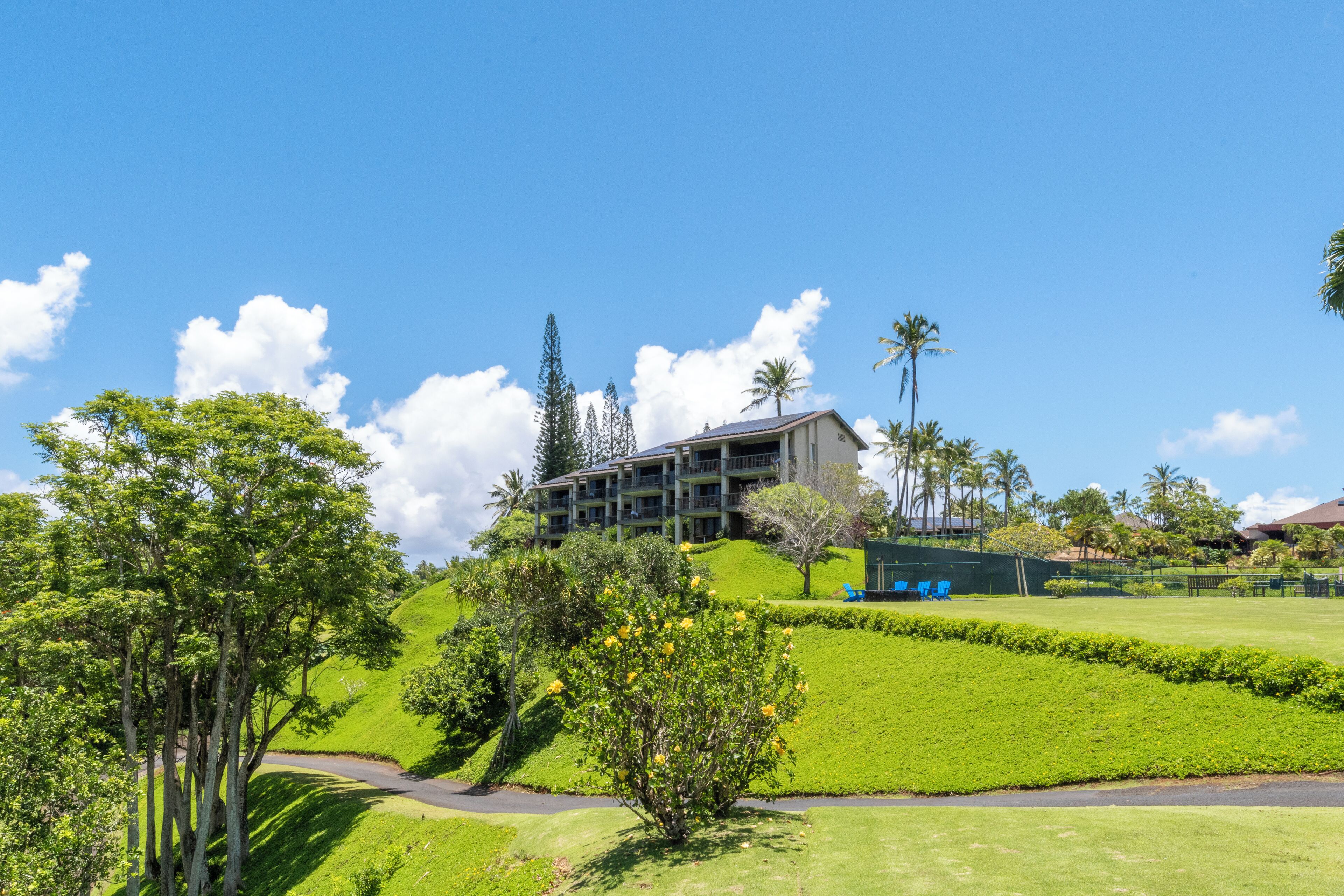 A hotel with a modern design, located on a green hill with a clear sky.