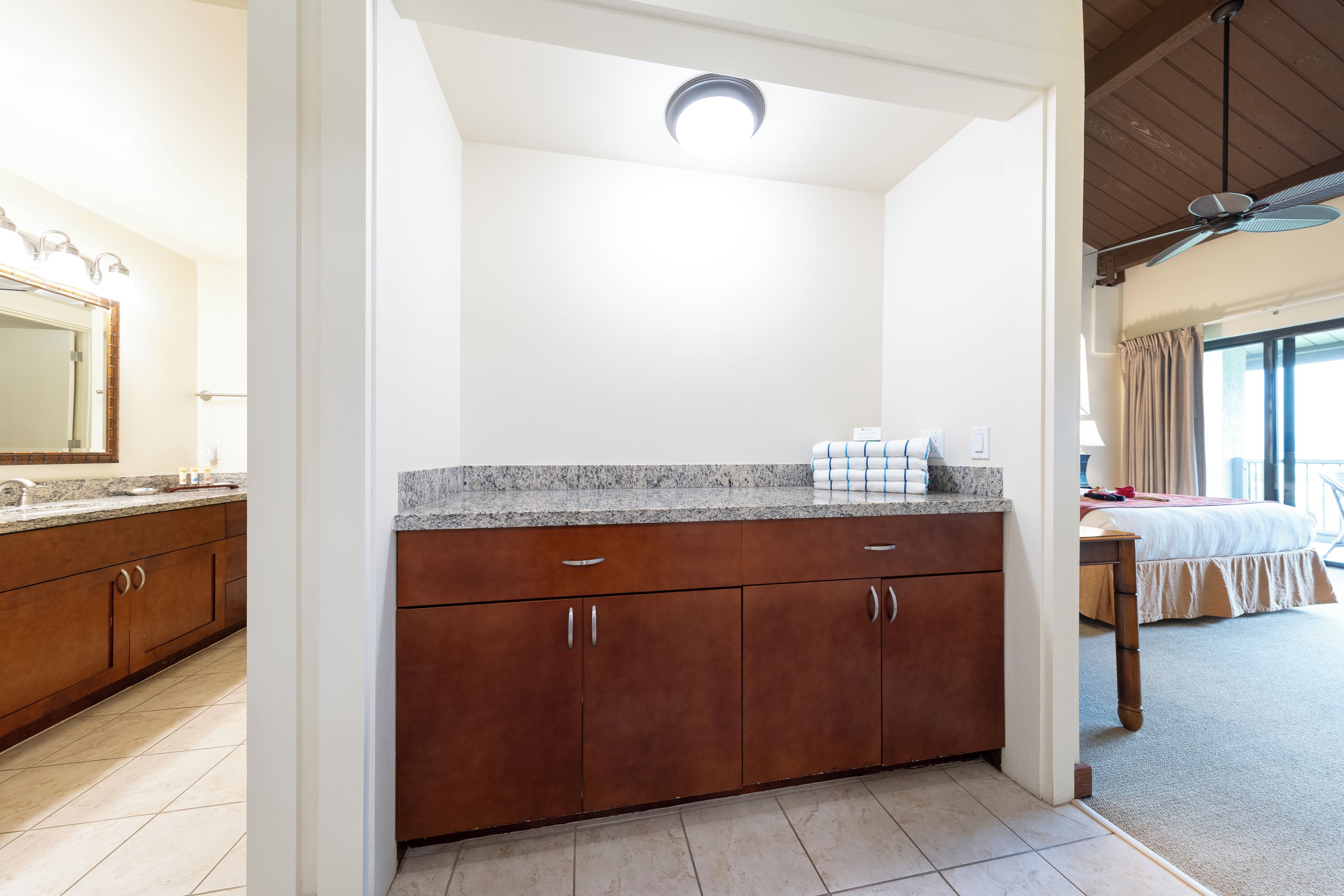 A hotel room with a bathroom, a kitchenette, a bed, and a ceiling fan.