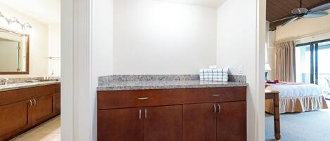 A hotel room with a bathroom, a kitchenette, a bed, and a ceiling fan.