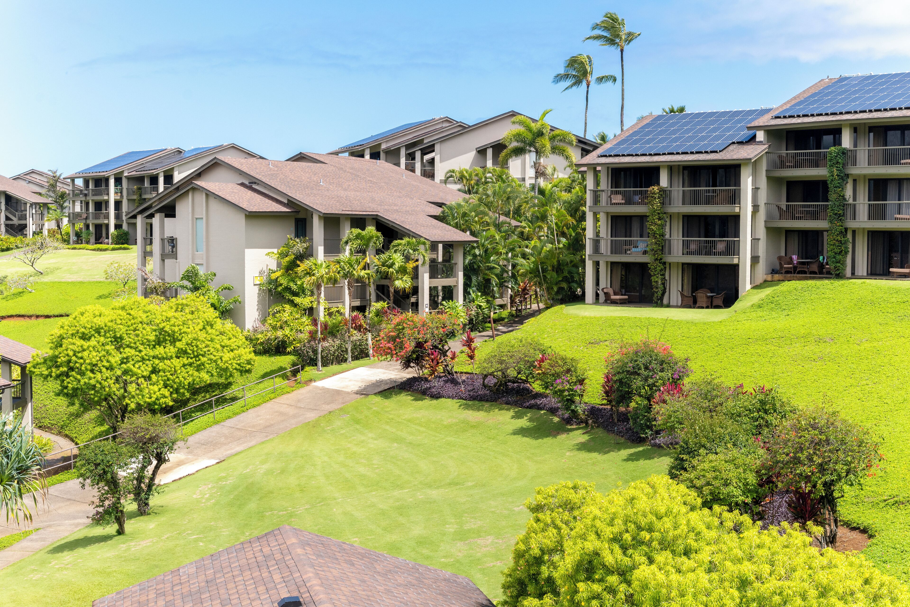 Un ensemble résidentiel composé de plusieurs immeubles à deux étages, dotés de panneaux solaires sur les toits, ainsi que de pelouses et de jardins bien entretenus.