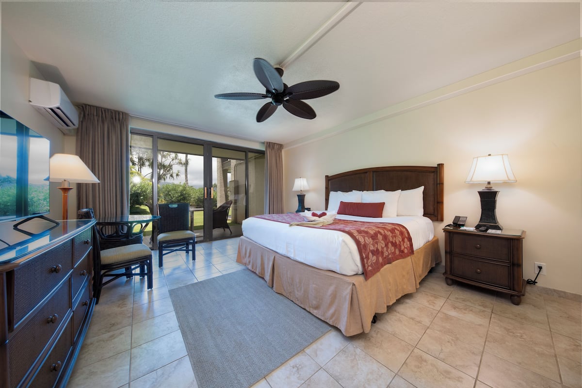 A hotel room with a bed, a desk, a chair, a nightstand, a lamp, and a ceiling fan.