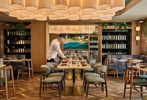 A restaurant with wooden furniture, a chef preparing food, and a mural on the wall. - Romer House Waikiki (Honolulu)