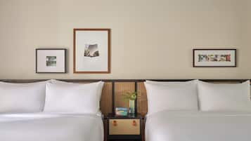 A hotel room with two beds, a nightstand with a vase of flowers, and three framed pictures on the wall.