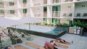 A group of people performing yoga on mats in an outdoor area with a pool and a multi-story building in the background. - Romer House Waikiki  (Honolulu)