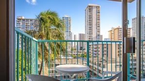 A balcony with a view of tall buildings, a palm tree, and a small round table with chairs. - Aqua Aloha Surf Waikiki (Honolulu)