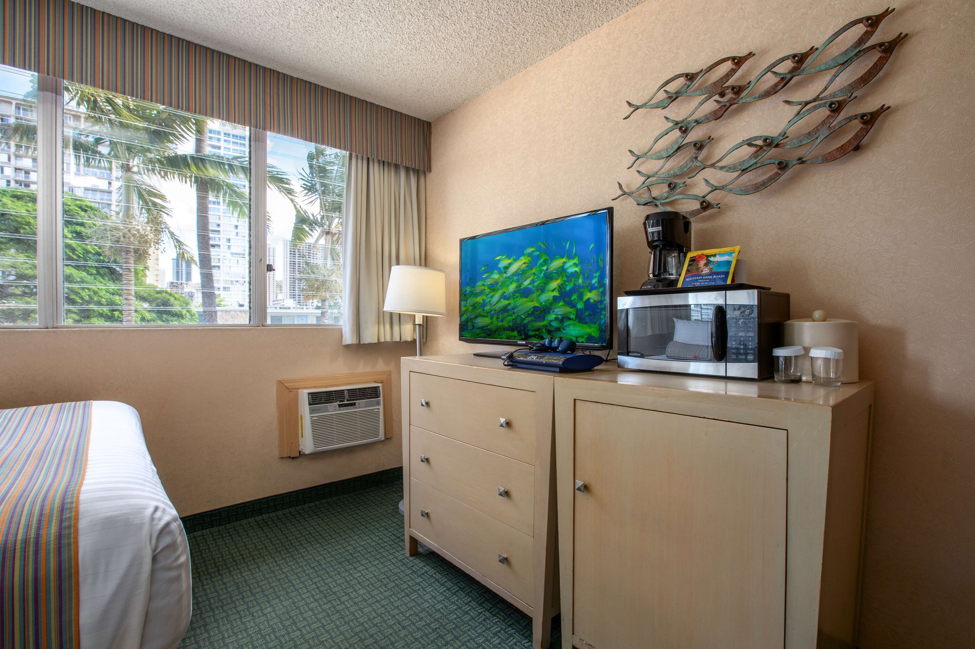 Une chambre d’hôtel équipée d’un lit, d’une télévision, d’une machine à café, d’un four à micro-ondes et d’une décoration murale représentant des poissons.
