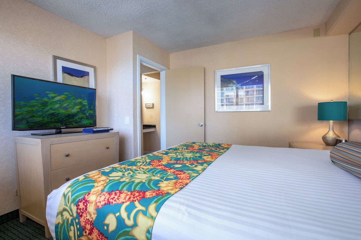 Een hotelkamer met een bed, een televisie op een dressoir, een raam en een deur die leidt naar een badkamer.
