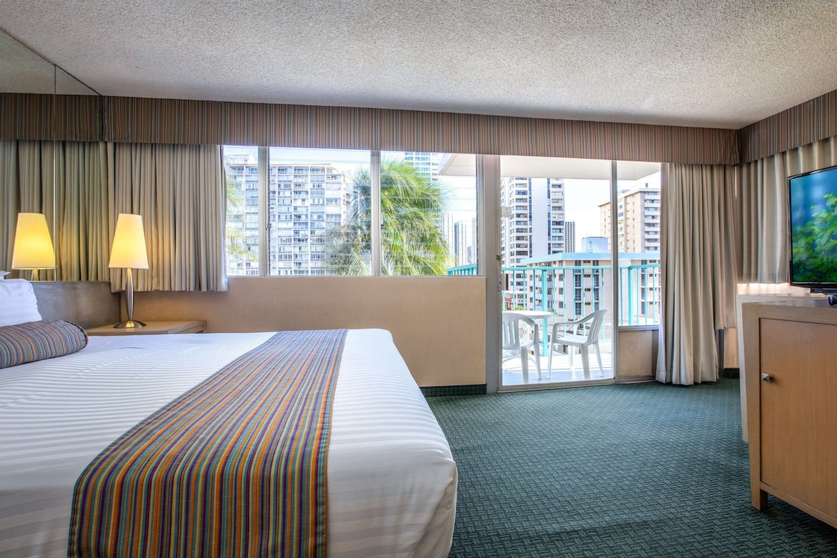Hotelkamer met een groot bed, een televisie, een bureau en een balkon met uitzicht op hoogbouw.