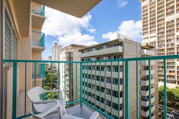 A balcony with white plastic chairs, a turquoise railing, and a view of adjacent high-rise buildings. - Aqua Aloha Surf Waikiki (Honolulu)