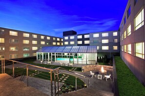 A modern building with a rooftop pool, outdoor seating, and a fire pit area.