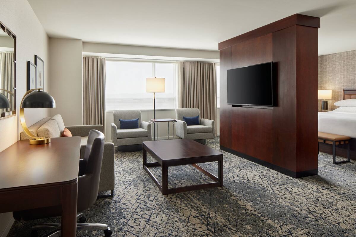 A hotel room with a desk, two armchairs, a sofa, a TV, and a bed.