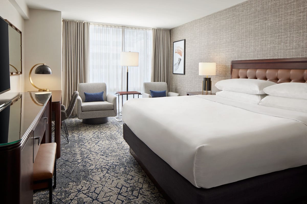 A hotel room with a large bed, two armchairs, a desk with a lamp, and a television.