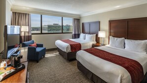 A hotel room with two beds, a desk with a coffee maker, a TV, and a view of the city.