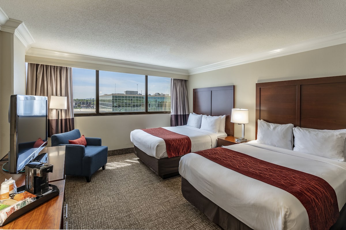 A hotel room with two beds, a desk with a coffee maker, a TV, and a view of the city.