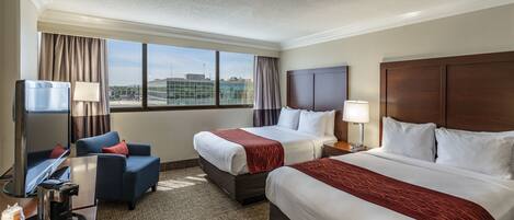 A hotel room with two beds, a desk with a coffee maker, a TV, and a view of the city.