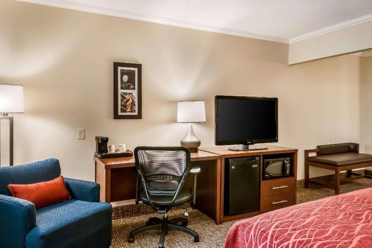 A hotel room with a bed, a desk with a computer, a chair, a television, and a small refrigerator.