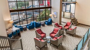A spacious lobby with a high ceiling, large windows offering a view of the street, and a staircase leading to an upper level.