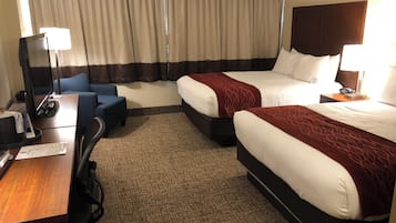 A hotel room with two beds, a desk, a chair, a lamp, and a TV.