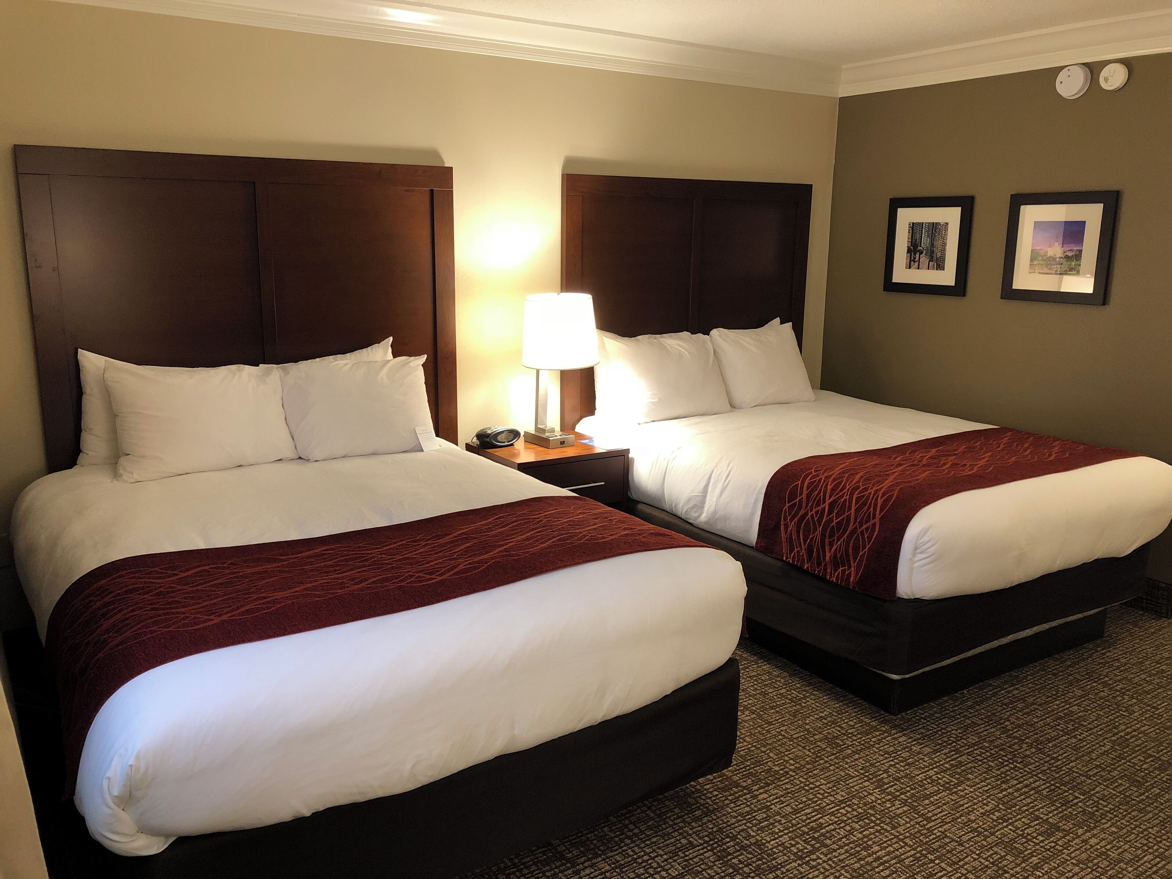 A hotel room with two beds, a nightstand with a lamp, and two framed pictures on the wall.