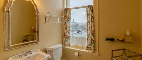 Un baño con lavamanos, inodoro y ventana con cortinas florales.